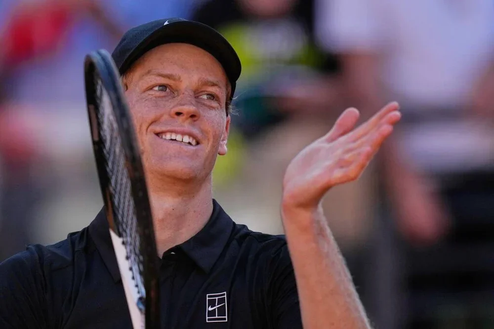 Jannik Sinner applauds the crowd at a tennis tournament wearing a black outfit.